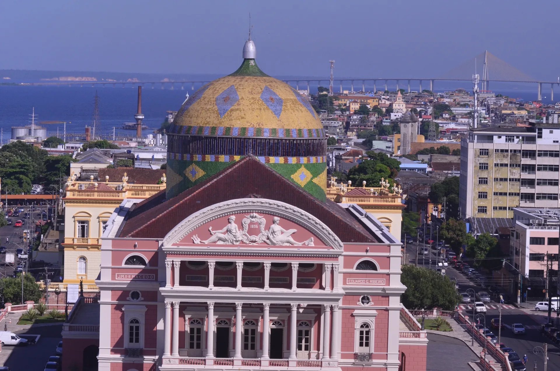 Cúpula colorida do Teatro Amazonas, com a fachada rosa e o Rio Negro ao fundo, em fotografia real de Ana Claudia Jatahy / MTur.