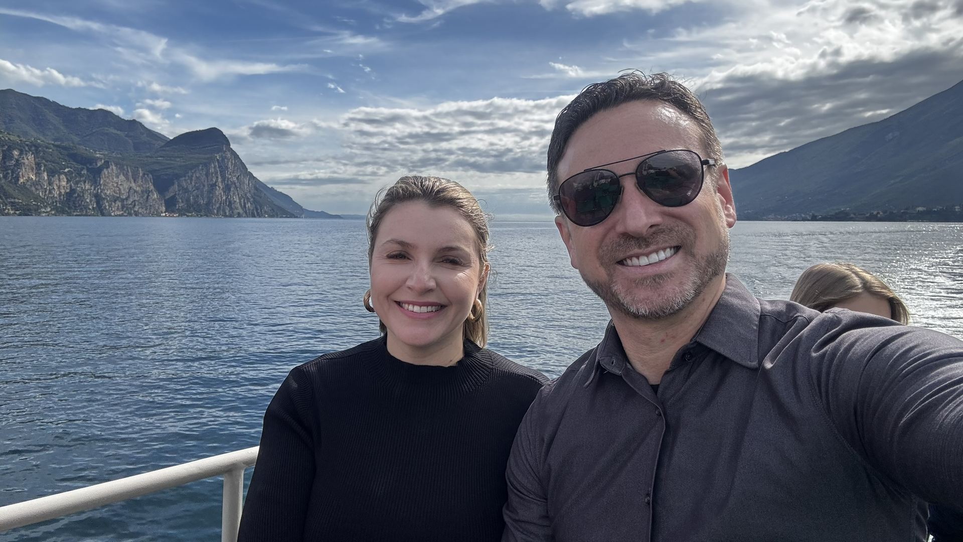 Marcelo e Alexandra de barco no Lago di Garda com montanhas ao fundo